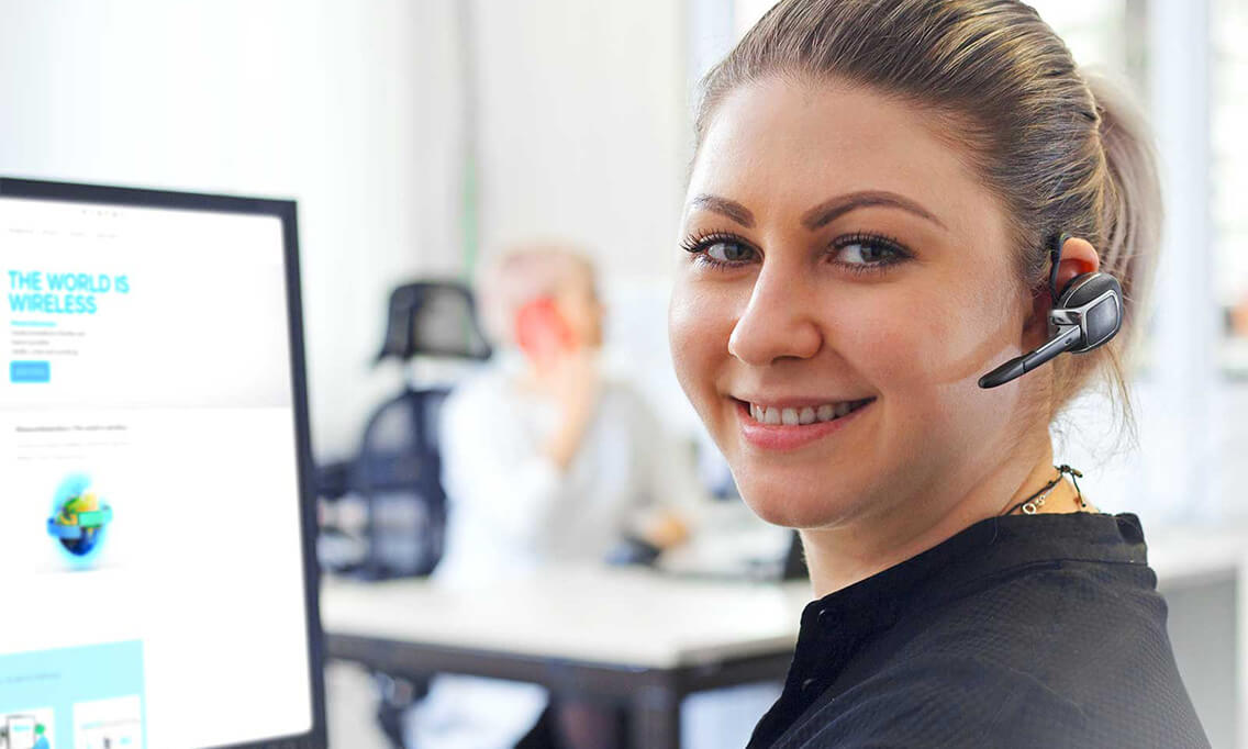 Woman with headset in front of a website about Industrial Wireless - Repair and Support at Schildknecht AG